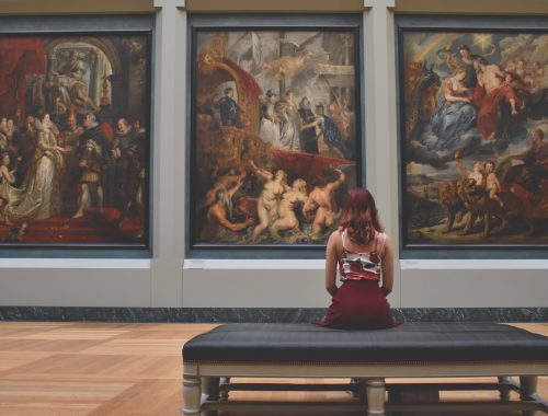 mulher sentada dentro de um museu de frente para três obras de arte