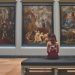 mulher sentada dentro de um museu de frente para três obras de arte