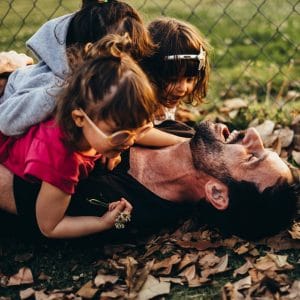 pai com filhas rindo abraçados no chão